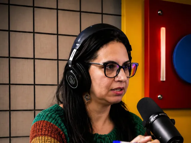 Renata Marques de óculos e fones, falando ao microfone num estúdio